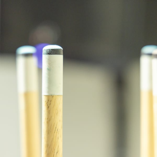 Close-up of three pool cues with light wooden shafts and white tips, against a blurred background.