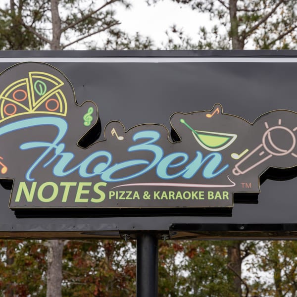 Frozen Notes Pizza & Karaoke Bar sign with neon pizza, martini, and microphone icons.