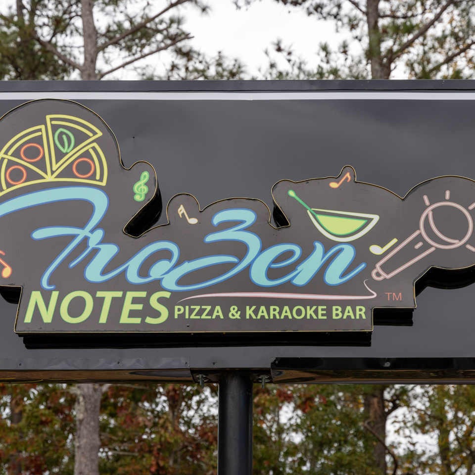 Frozen Notes Pizza & Karaoke Bar sign with neon pizza, martini, and microphone icons.