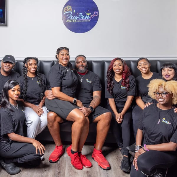 Nine smiling staff members in black shirts with the Frozen Notes logo, seated and kneeling.