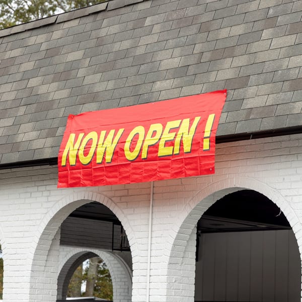 A red banner with yellow text "NOW OPEN!" hangs above white brick arches of Frozen Notes.